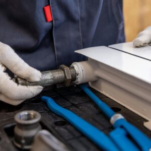 Close-up of a plumber installing a radiator pipe using specialized tools.